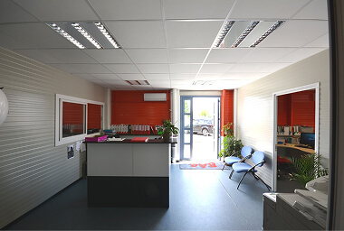 Clean office reception with black and white desk, visitor chairs, shelves with folders, and natural light from a glass door, creating a professional and welcoming environment.