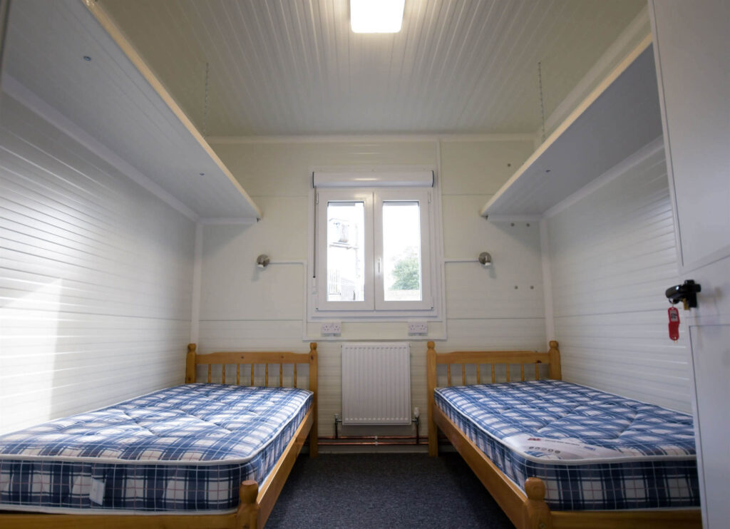Small bedroom with two single wooden beds, blue checkered mattresses