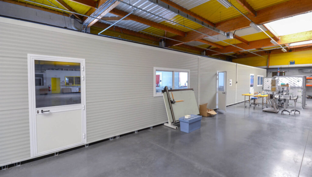 Interior of industrial workshop with modular panel structure, multiple doors and windows.