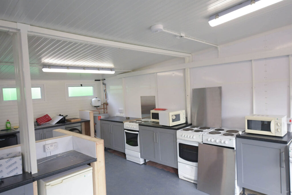 Organized kitchen with two white electric stoves, microwaves on countertops, gray cabinets, refrigerator, sink with dish rack