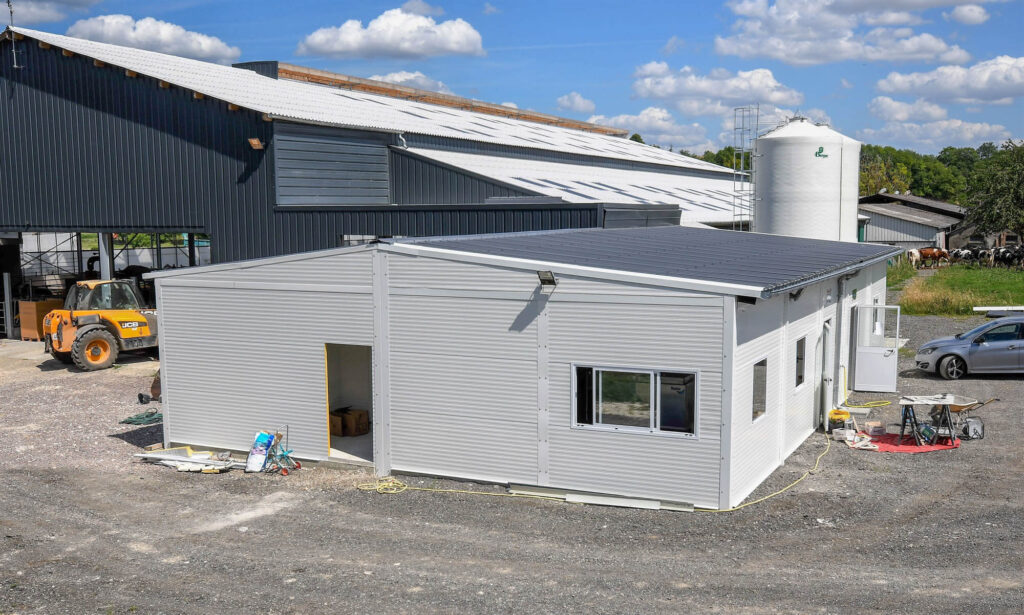 Light gray modular building with dark roof on gravel lot, surrounded by tools and construction materials.