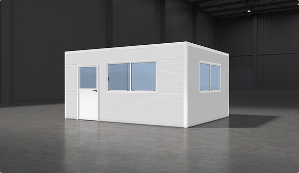 Small rectangular modular office with white paneling, windows, and door placed inside large industrial warehouse with concrete floor and high ceiling.